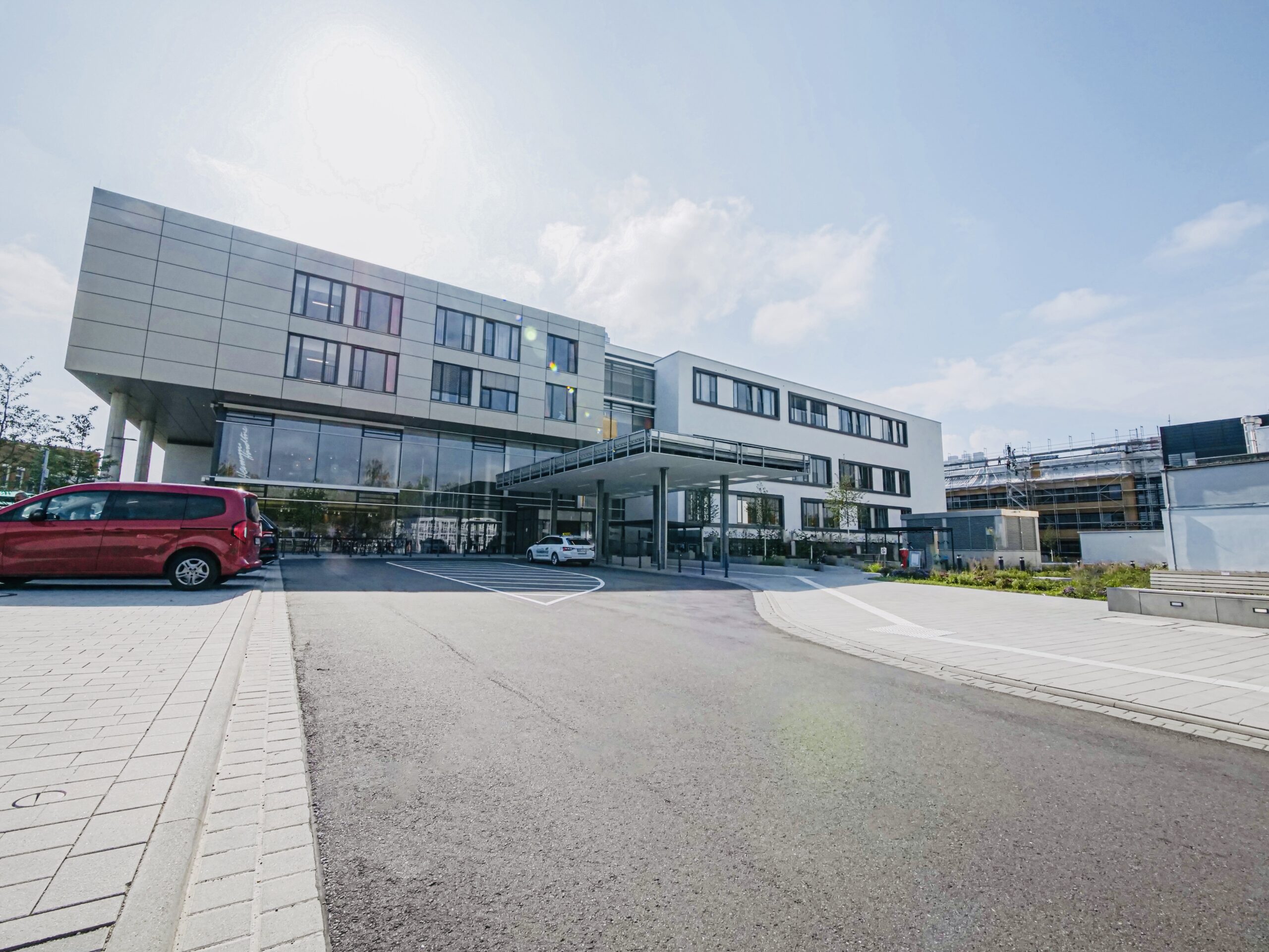 Moderne Klinik mit mehrstöckigem Gebäude, großem Eingangsbereich und parkenden Autos im Vordergrund.